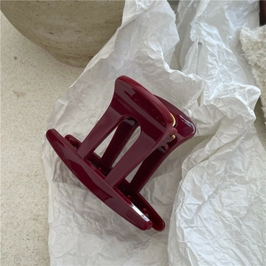 Dettaglio di un fermaglio per capelli bordeaux in plastica lucida con molla dorata