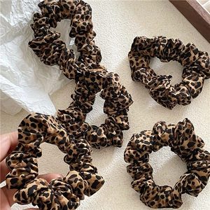 Detail of four pleated leopard print satin hair scrunchies on a white surface