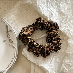 Detailed close-up of leopard print scrunchie on white textured paper with artistic bowl