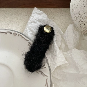 Close-up of a black plush hair clip with golden metallic POKO TDSCA button detail
