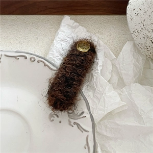 Detail of dark brown plush hair clip with golden metal logo on vintage ceramic saucer