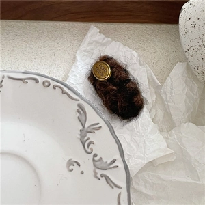 Detail view of coffee plush hair clip with vintage golden metal plate on white surface
