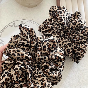 Close-up of oversized leopard print hair scrunchies on a textured white ceramic plate