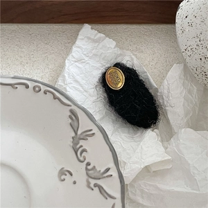 Detailed close-up of a plush black fabric hair clip with a golden oval metal brand plate