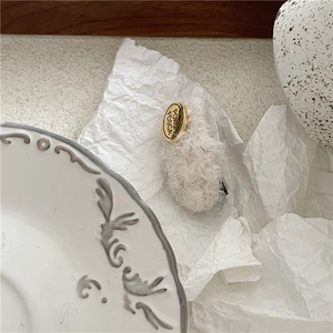 Detailed close-up of cream plush rectangular hair clip with engraved gold metal emblem