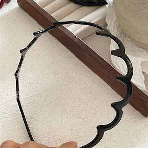 Detail shot of a slim black wavy headband with a glossy finish for hair styling