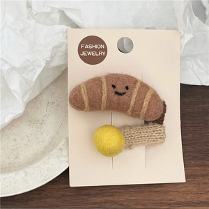 Close-up of wool felt croissant hair clip with smile face and yellow ball on card