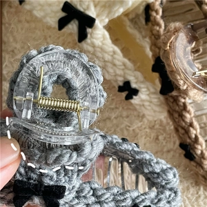 Detail of grey knitted hair claw clip featuring a black velvet bow and golden spring mechanism