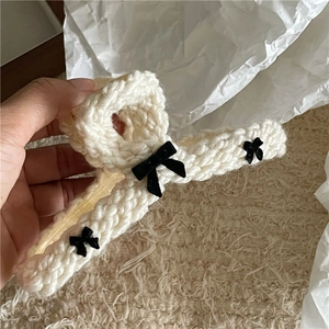 Detailed close-up of knitted cream wool hair claw clip with black satin bow accents