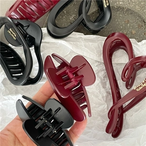 Detail view of large resin hair claws in burgundy and black with gold logo accents