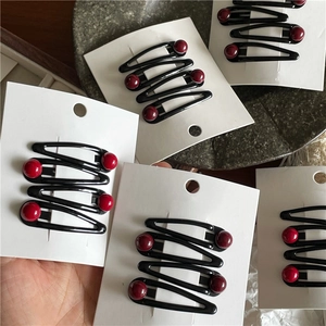 Detail of red bead and black wavy metal BB hair clips set on white card display
