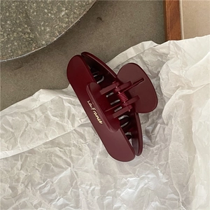 Close-up of matte burgundy hair claw clip with golden lettering on textured white paper
