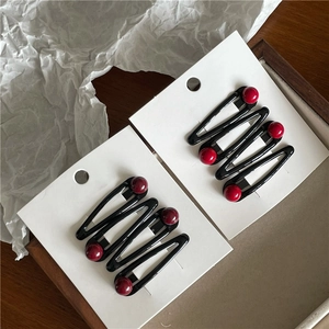 Detail showing wave-shaped black metal BB hair clips with shiny red beads on white card