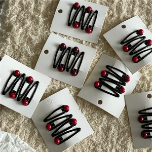 Detail of black metal BB hair clips with red round beads on a beige texture background