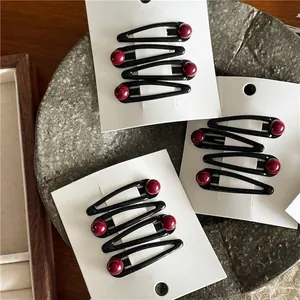 Set of four black teardrop hair clips with dark red beads on a white display card