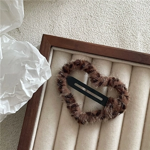 Macro view of brown plush heart-shaped hair clip with black metal snap closure