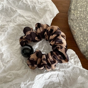 Détail du chouchou à motif léopard en tissu avec une perle noire élégante
