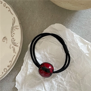 Detail view of a black elastic hair tie with a glossy red and black marbled resin bead