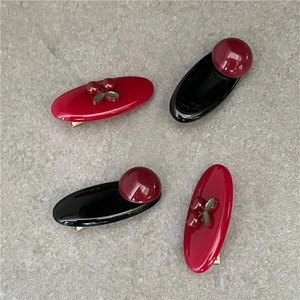 Detailed view of red cherry hair clips and glossy beads on oval snap hairpins for girls