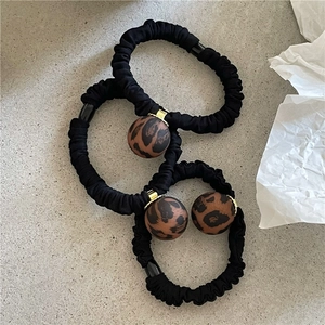 Detailed view of three leopard print ball hair ties on black ruffled elastic scrunchies