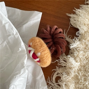 Detail of wool felt pizza hair tie with brown spiral band on a cozy wooden desk