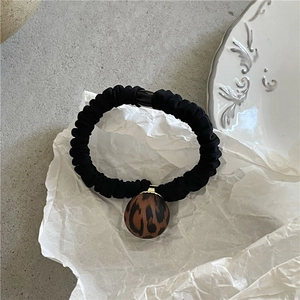 Close-up of black pleated scrunchie with leopard print charm on artistic white paper