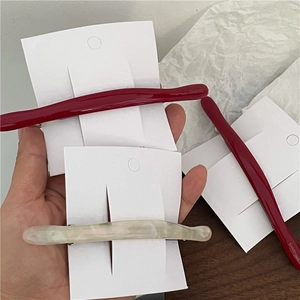 Close-up of curved acetate hair clips in deep red and pearly white on display card