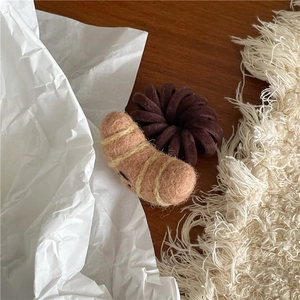 Close-up of handmade wool felt croissant hair tie on a rustic wooden surface