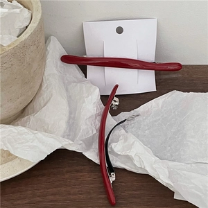 Detailed macro view of two minimalist deep red curved hair clips with a glossy finish