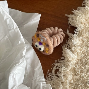 Close-up of a handmade wool felt brown bear charm on a pink spiral telephone wire hair tie
