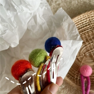 Close-up of colorful wool felt ball hair clips on a textured metal BB clip base