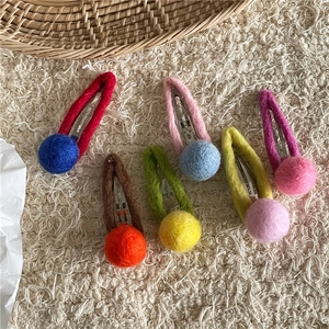 Detail of wool felt ball hair clips in diverse colors on a soft white texture background