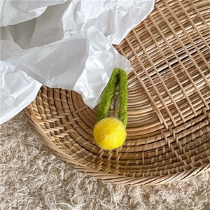Detail of a handmade yellow wool felt flower hair clip on a woven bamboo tray base