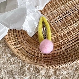 Detail of handmade wool felt hair clip with yellow ring and pink pompom on woven basket