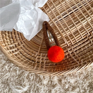 Detail view of handmade brown wool felt hair clip with orange pompom on woven tray