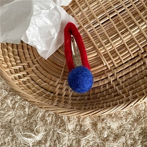 Detail of red knitted loop hair clip with blue pom pom on a metal duckbill base