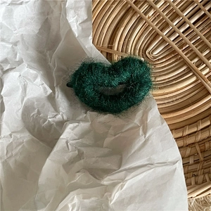 Gros plan d'une pince à cheveux en laine vert foncé en forme de cœur sur un plateau tissé