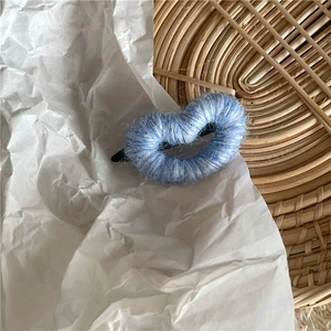 Gros plan sur une pince à cheveux cœur en laine bleu ciel sur papier blanc et rotin
