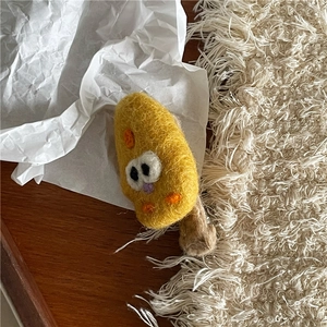 Nahaufnahme der gelben Filz-Haarklammer in Käse-Optik mit Cartoon-Augen auf Holzdekor