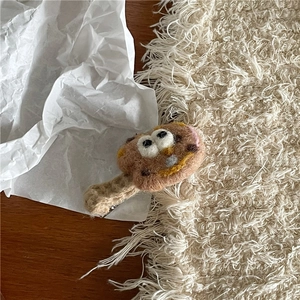 Makroaufnahme einer handgemachten Wollfilz-Kekshaarspange mit Augen auf Holzgrund
