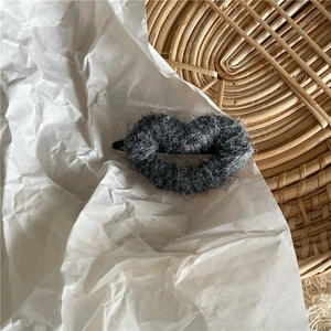 Détail d'une pince à cheveux cœur en peluche grise sur papier et fond en osier tressé