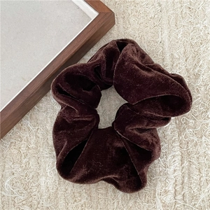 Detail eines dunkelbraunen Samt-Scrunchies mit weicher Faltung auf beigem Gewebe