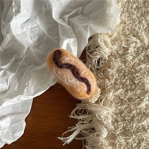 Nahaufnahme der handgemachten Wollfilz-Hotdog-Haarklammer mit gestrickter Basis auf Tisch