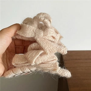 Close-up of beige knitted bow hair claw clip showing soft yarn texture and metal spring