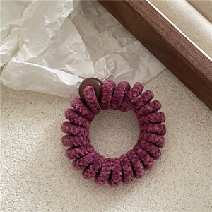 Détail d'un élastique spirale en velours violet foncé avec une perle sur bois
