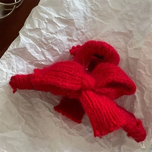 Detail showing red knitted bow hair clip on a minimalist white textured backdrop