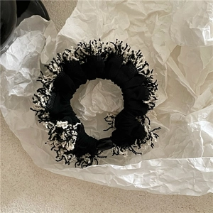 Detail of a monochrome fringe scrunchie with plush tufted texture on white paper