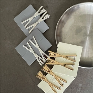 Dettaglio di fermagli per capelli a X in lega nei colori oro e argento su cartoncini