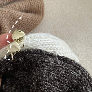 Détail d'un pendentif cœur doré sur tissu en maille montrant la texture polie et la couture