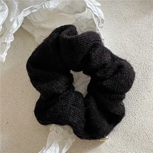 Gros plan du chouchou en maille noire avec un petit pendentif coeur doré sur papier blanc